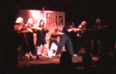 Animated clip of seven Amelias on stage performing a dance in unison where they hold their arms out and push forward three times as if diving into a pool, and then wrap their bodies around to the other side and raise their arms up.