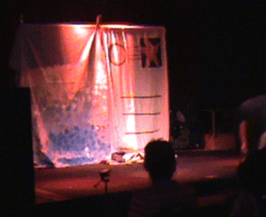 an animated clip from the play, first we see an empty stage, then suddenly one Amelia crashes into it and rolls with a dramatic tumble, followed by a wave of 4 or 5 more amelias all crashing and rolling onto the stage.